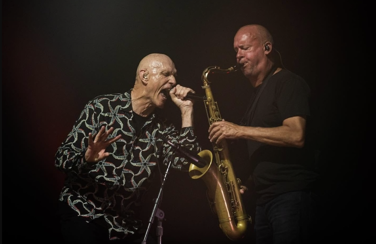 Peter Garrett singing into a microphone alongside a saxophone player during a live concert performance by Midnight Oil.